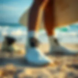 A surfer showcasing different types of surfing booties on a sandy beach